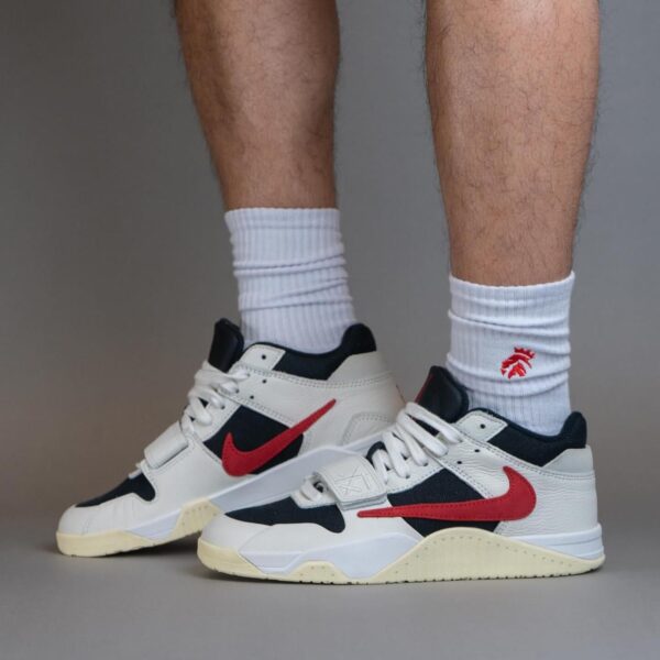 Pair of white and navy sneakers with red Nike swooshes, worn with white crew socks, standing on a gray surface.