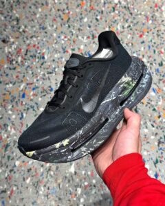 Black athletic sneaker with a marble-patterned sole, held in a hand against a speckled background.