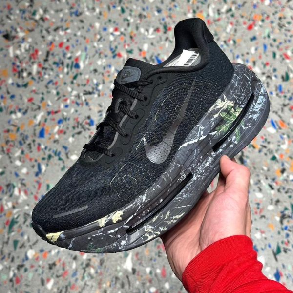 Black athletic sneaker with a marble-patterned sole, held in a hand against a speckled background.