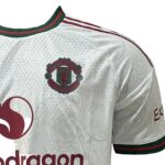511d314f-bcd4-4b1f-9724-fd97dae5893e | UAE SPORT STORE White Manchester United football jersey with club crest on chest and red sponsor logo, green/red trim at collar and sleeves.