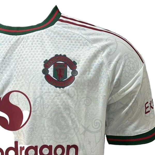 White Manchester United football jersey with club crest on chest and red sponsor logo, green/red trim at collar and sleeves.