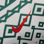 Close-up of a red Nike swoosh embroidered on a white fabric with teal geometric pattern.