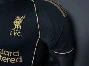Close-up of a dark navy Liverpool FC jersey showing the gold club crest and 'Standard Chartered' sponsor.
