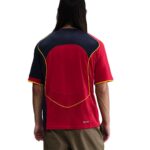 Back view of a red and navy athletic jersey with yellow piping, worn by a person in tan shorts.