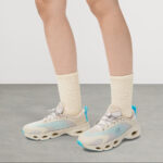 Pair of light beige and aqua athletic sneakers with cream socks, shown on a gray floor from the calves down for a fashion/footwear look.