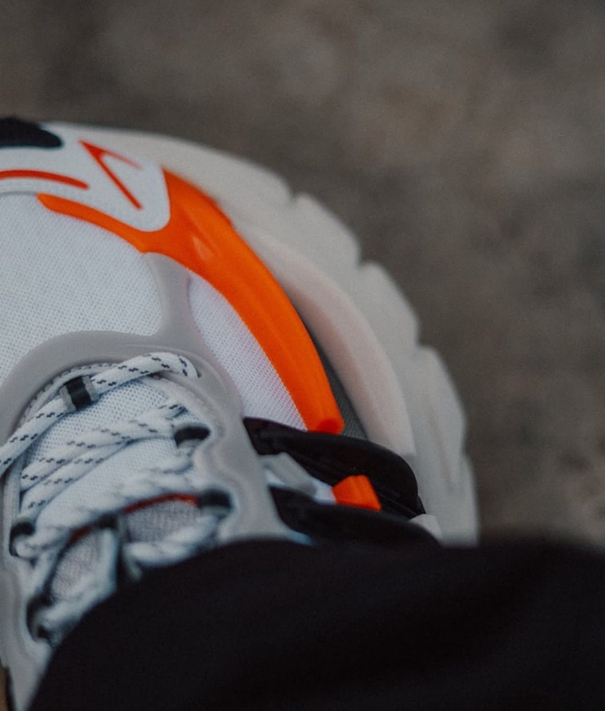 Close-up of a white running shoe with orange accents and white laces visible in the foreground, showing the toe area and a bright orange stripe/shell.