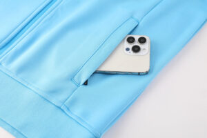 51fecec2 | UAE SPORT STORE Blue hoodie pocket with a smartphone partially tucked inside, showing the phone's triple-camera layout (informative).