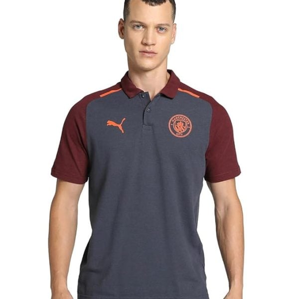 Model wearing a gray-blue polo shirt with maroon sleeves featuring a Manchester City crest and orange Puma logo on the chest.