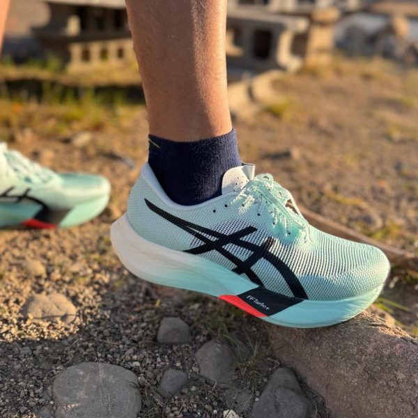 Teal running shoe on a rocky trail, close-up of laces and white sole, with a dark sock visible above the shoe.