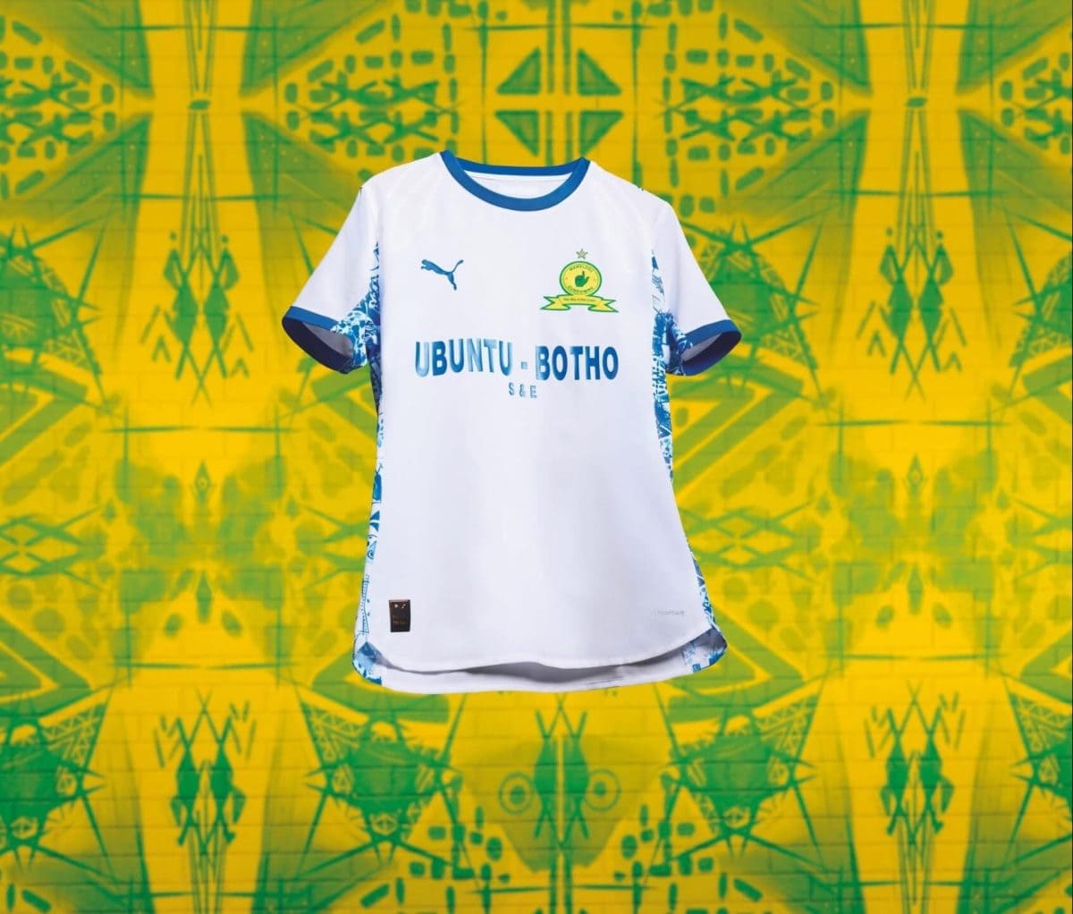 White soccer jersey with blue trim and crest appears suspended against a neon yellow‑green abstract mural; reads 'UBUNTU BOTHO' across the chest.