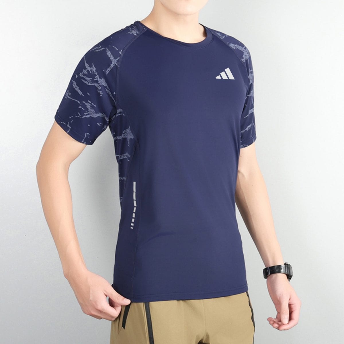 Man wearing a navy athletic shirt with a white marble pattern on the shoulders and sleeves, paired with tan shorts with black zippers.
