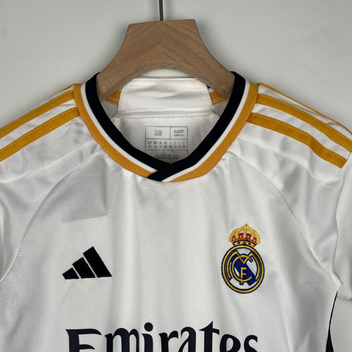 White Real Madrid soccer jersey on a wooden hanger, featuring the club crest and the Adidas logo.