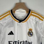 White Real Madrid soccer jersey on a wooden hanger, featuring the club crest and the Adidas logo.