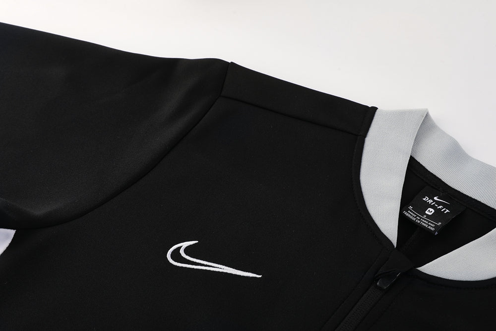 52d59444 | UAE SPORT STORE Close-up of a black Nike Dri-FIT athletic jacket with a light gray collar and a white embroidered swoosh on the chest area.