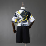 Back view of a mannequin wearing black shorts and a short-sleeve graphic tee with black, white, and yellow abstract design.