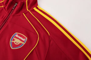 Red Arsenal jacket close-up showing yellow piping and club crest on the chest, highlighting colors and badge