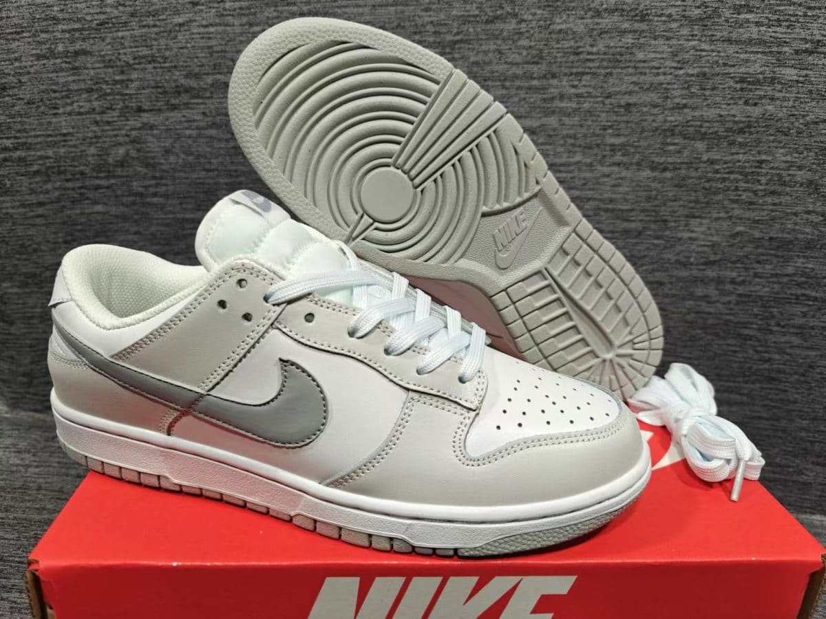 White and light-gray Nike sneakers resting on a red Nike shoebox, close-up of side profile and treaded sole nearby