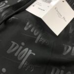 Black fabric with a subtle gray repeating Dior logo and a white Christian Dior Paris tag attached, suggesting a Dior item.