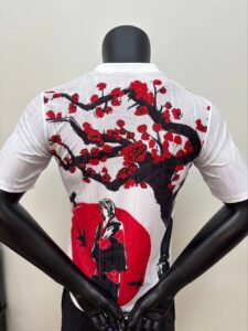 White shirt back with a large black and red cherry blossom tree graphic and a red sun motif, featuring a stylized figure beneath the tree