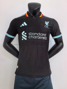Front view of a black Liverpool FC polo shirt on a mannequin, featuring a crest, light blue trim on sleeves, and the Standard Chartered sponsor logo in white/blue.