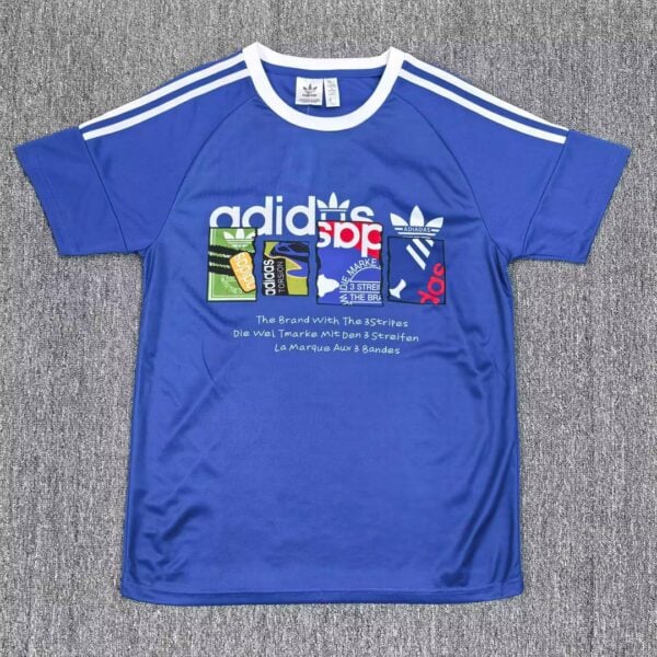 Blue Adidas T-shirt with white collar and three white stripes on the shoulders, featuring a multicolored block graphic and brand text on the chest.