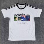 White Adidas t-shirt with black stripes on the shoulders and a multicolor logo collage across the chest.
