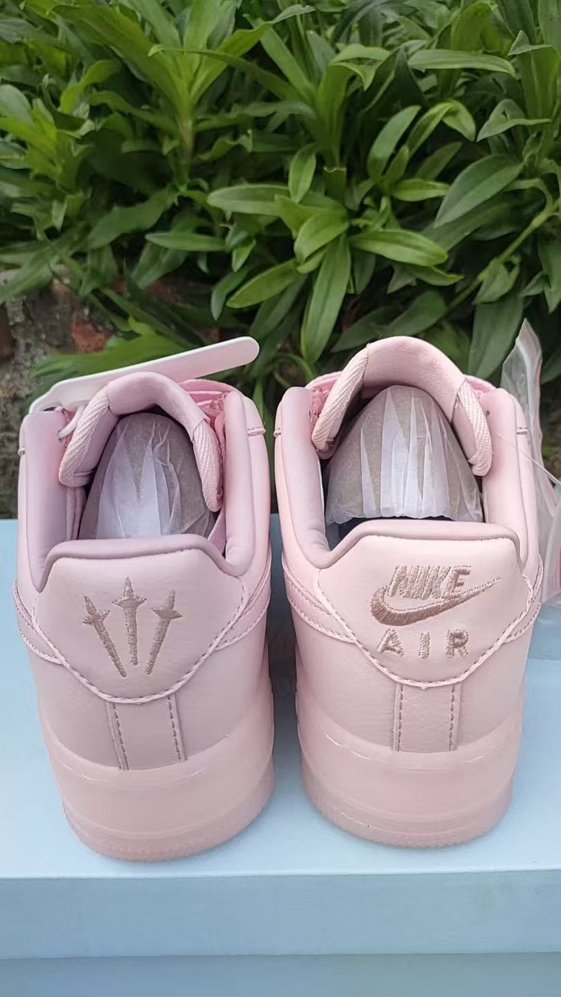 5450d5c9 | UAE SPORT STORE Pair of light pink Nike Air sneakers, shown from the back on a blue surface with green plants in the background.