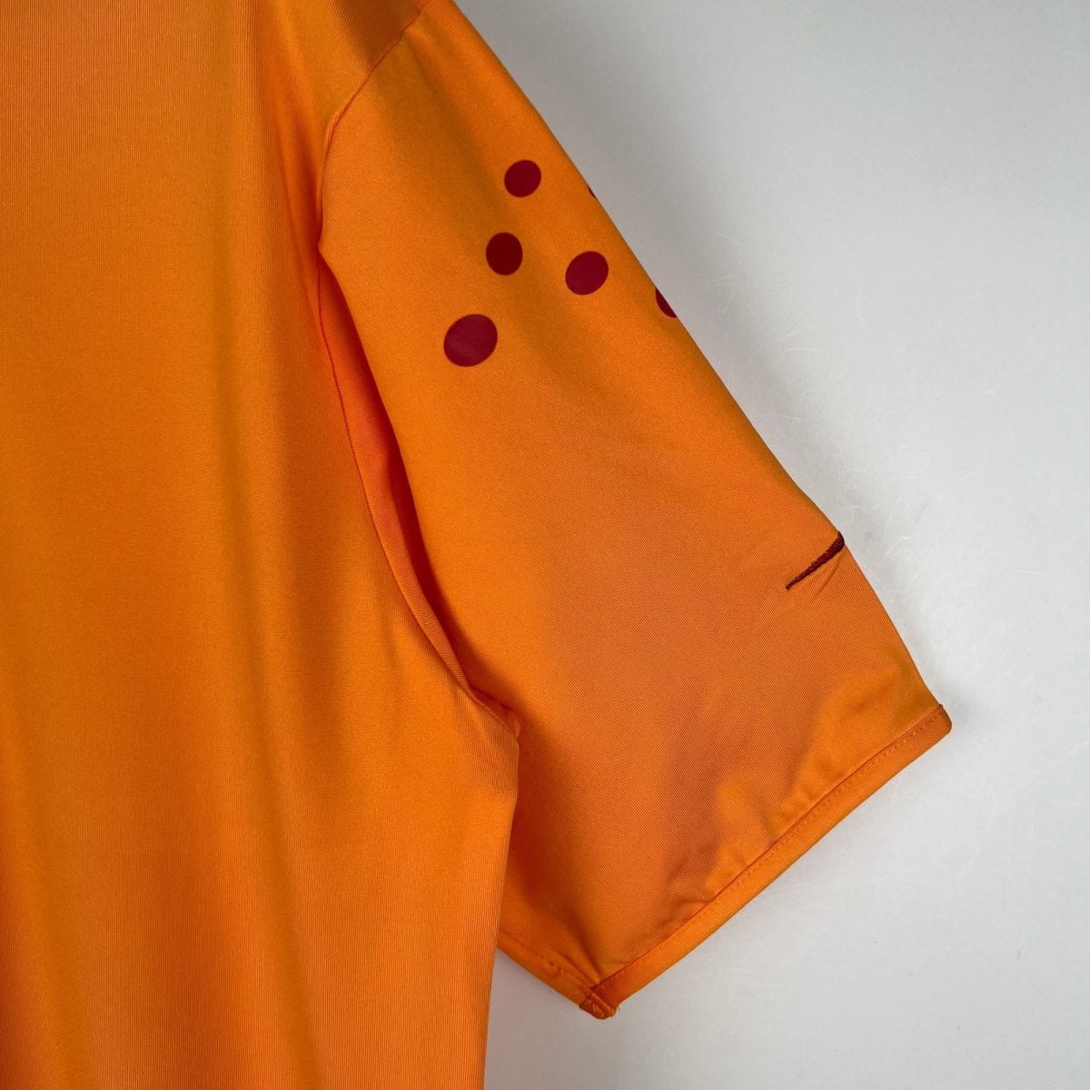 Close-up of orange fabric with red polka-dots along the sleeve seam without showing the full garment.