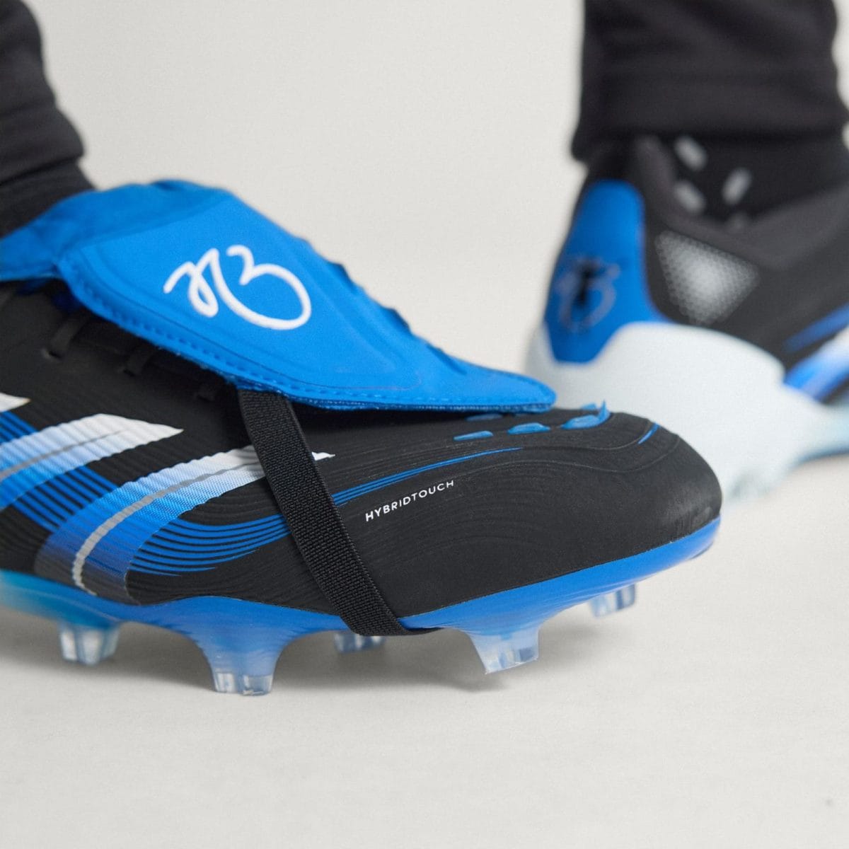 Close-up of blue and black soccer cleat with studs, highlighting HYBRIDTOUCH branding on the side.
