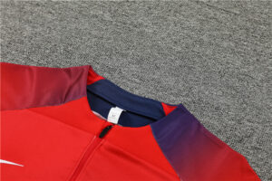 553cb6e4_1024x1024_2x_1b0562f1-d677-4399-a7b5-cde42d0d5794 | UAE SPORT STORE Red zip-up jacket with purple shoulder panels and navy collar, size M, laid on gray carpet.