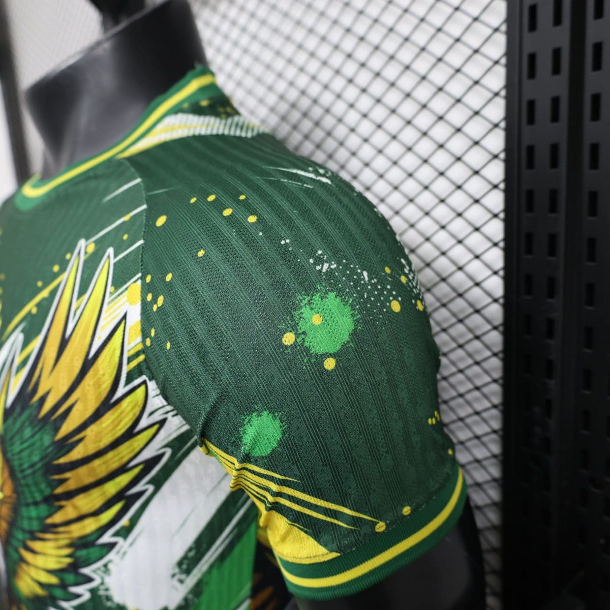 Close-up of a green sports jersey with yellow paint splatters and stripes, against a chain-link background.