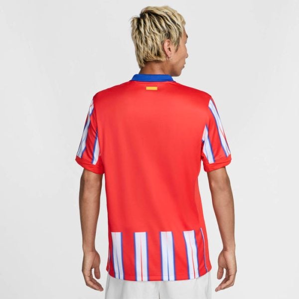 Person viewed from behind wearing a red soccer jersey with blue collar and vertical white-blue stripes on the sides and sleeves.