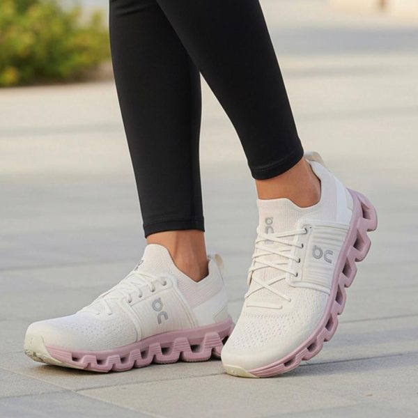 White athletic sneakers with a pink segmented sole on a gray sidewalk, worn with black leggings.