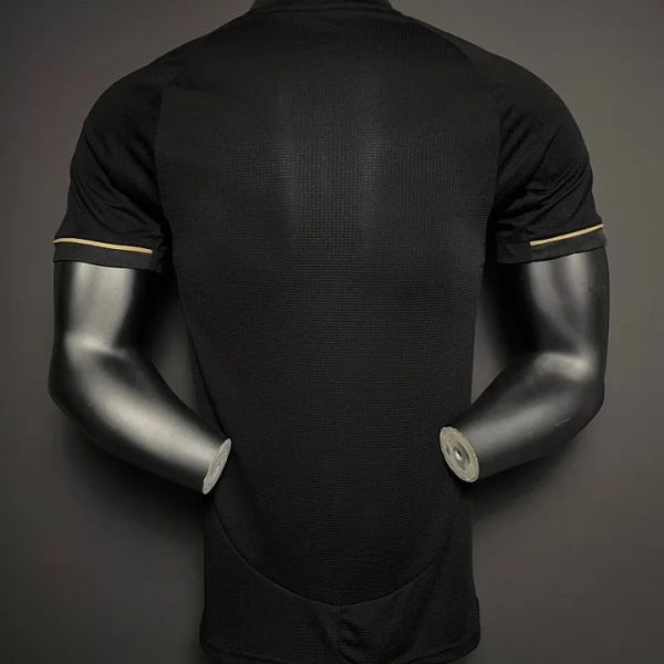 Back view of a black short-sleeve athletic shirt on a mannequin, showing subtle tan piping near the sleeve cuffs.