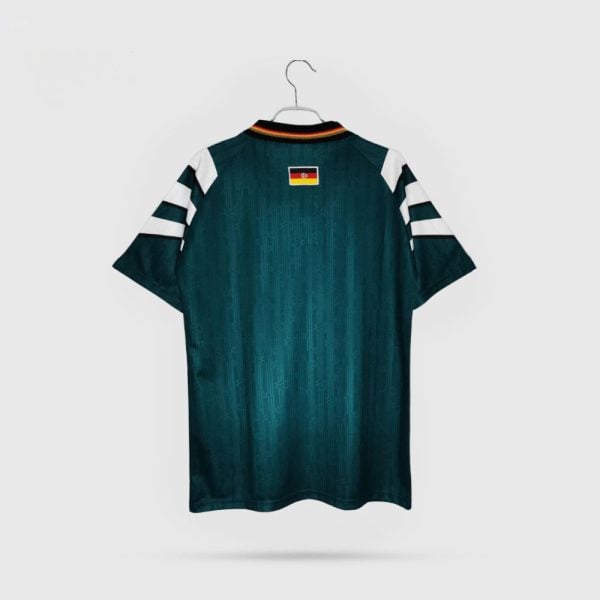 Teal soccer jersey with white striped sleeves, hanging on a hanger, small flag patch at the upper back neck area.