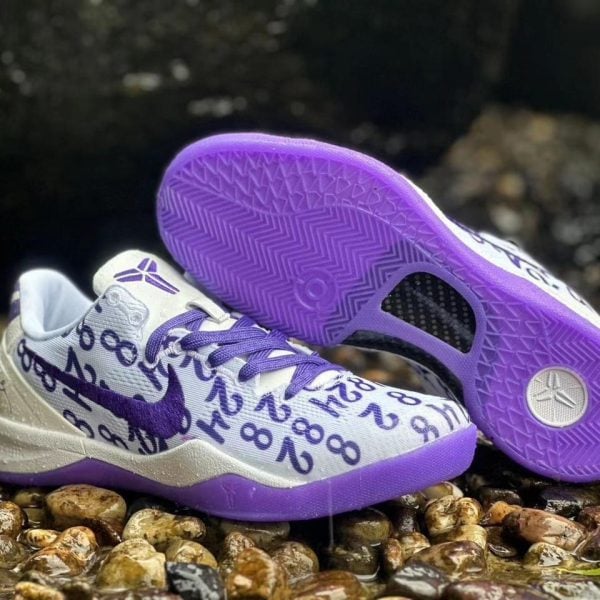 White and lavender athletic sneakers with a purple sole, resting on wet pebbles; upper covered in a purple numeric pattern.