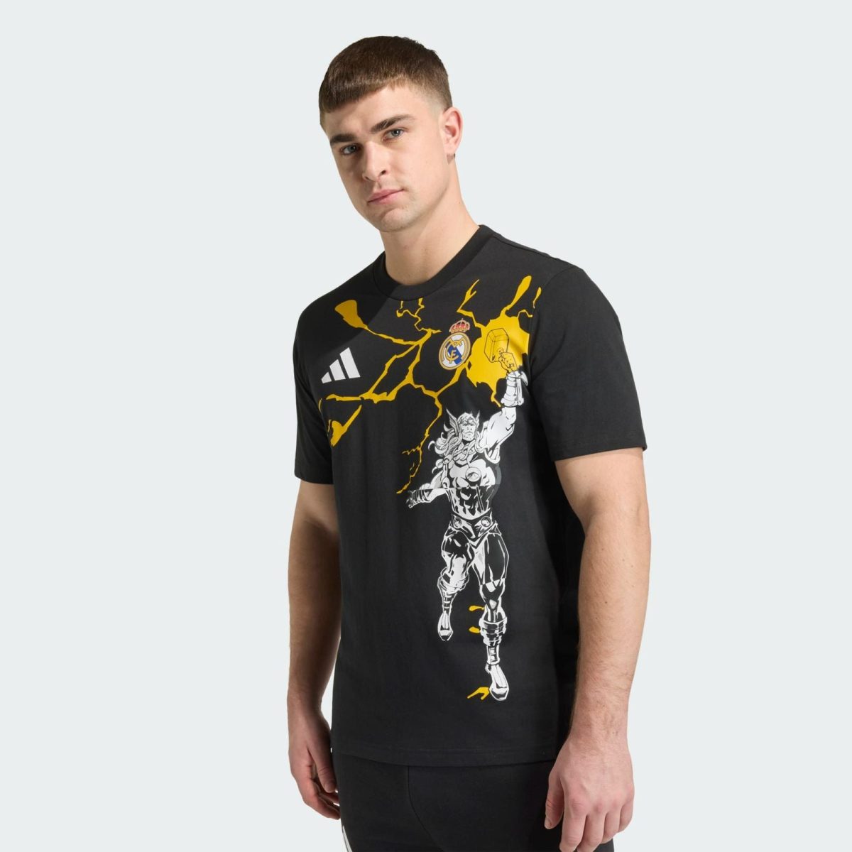 Model wearing a black graphic T-shirt with yellow crackle design and a white illustrated figure, standing against a light background.