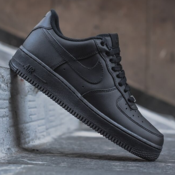 Black Nike Air Force 1 sneaker perched on a concrete step, showing the side and sole with the Nike Swoosh