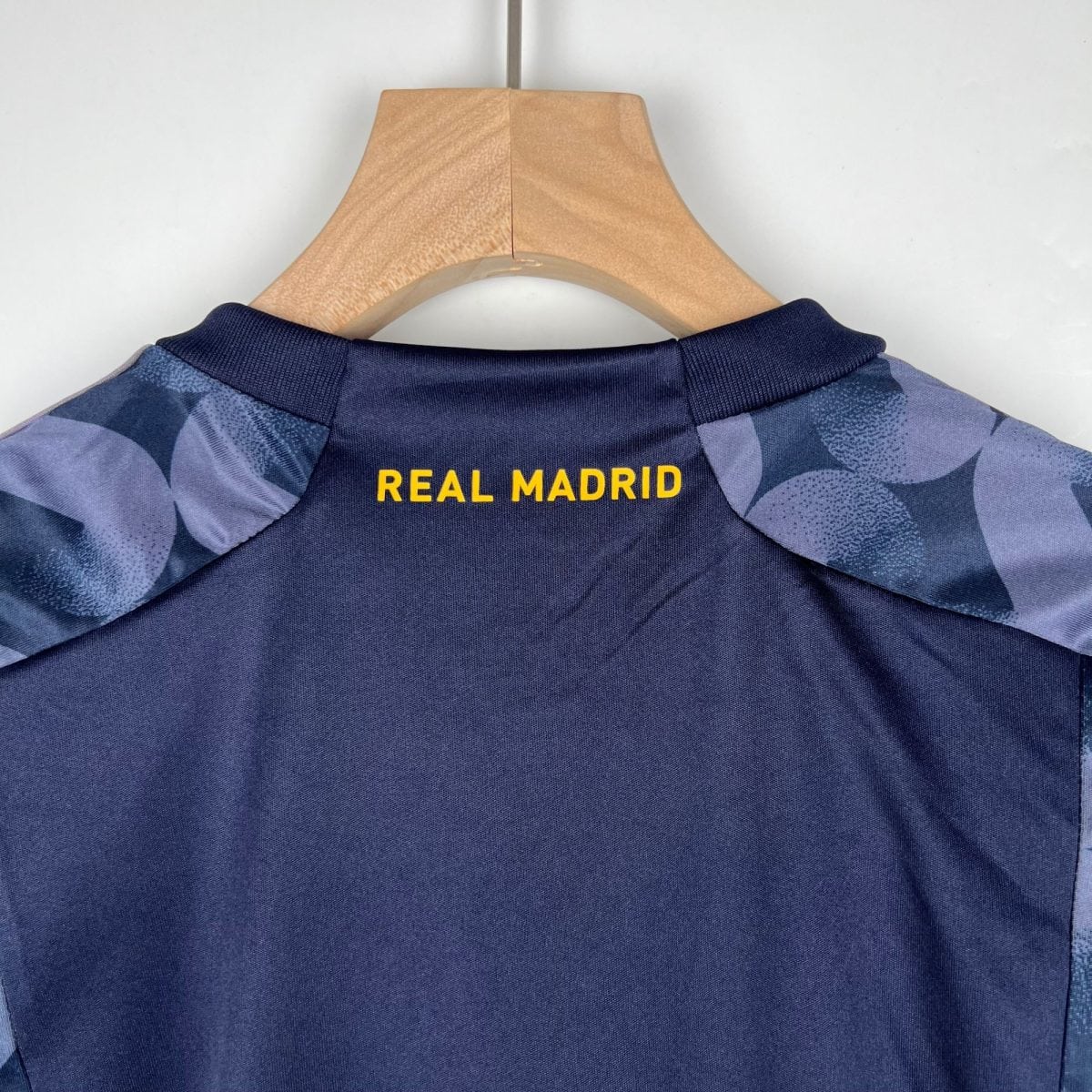 Navy blue Real Madrid shirt on a wooden hanger, with the yellow words REAL MADRID visible at the back near the collar