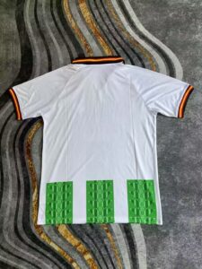 White polo shirt laid flat, with striped black-red-gold collar and sleeve trim, and three green patterned blocks at the hem on the back.