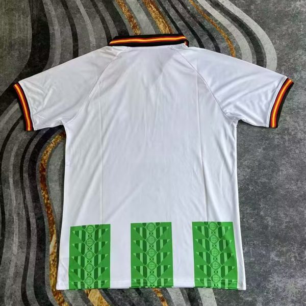 White polo shirt laid flat, with striped black-red-gold collar and sleeve trim, and three green patterned blocks at the hem on the back.
