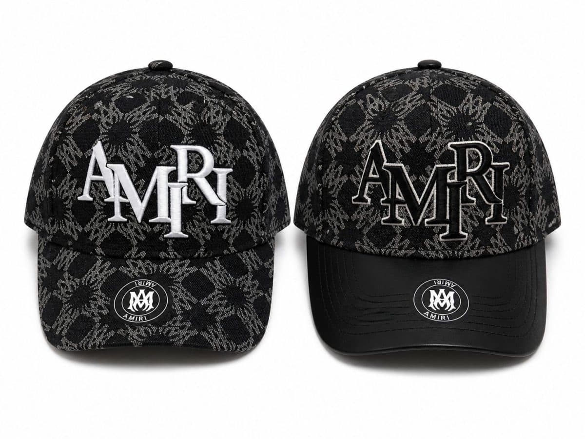 Two black caps with a gray jacquard pattern and AMIRI branding, one with solid white 'AMIRI' embroidery and the other with outlined embroidery on the front panels.