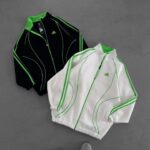 Two Adidas track jackets (black and white) with neon green piping laid on a gray surface.