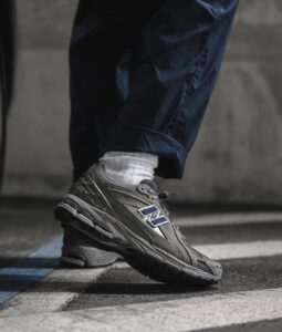 Close-up of a gray New Balance running shoe stepping over a blue-and-white painted line on pavement, with a white sock showing beneath navy pants.