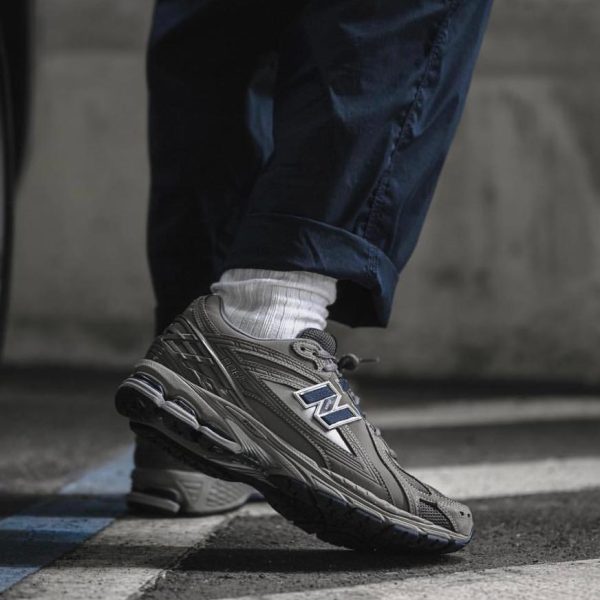 Close-up of a gray New Balance running shoe stepping over a blue-and-white painted line on pavement, with a white sock showing beneath navy pants.