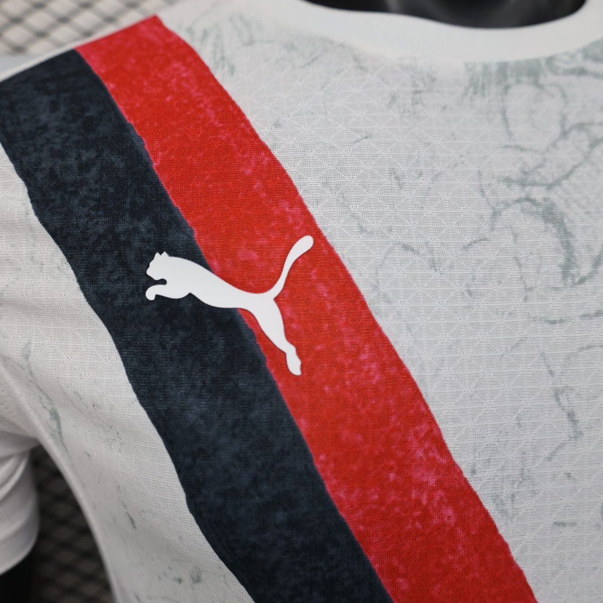 Close-up of fabric with red and dark blue stripes and a white Puma silhouette logo.