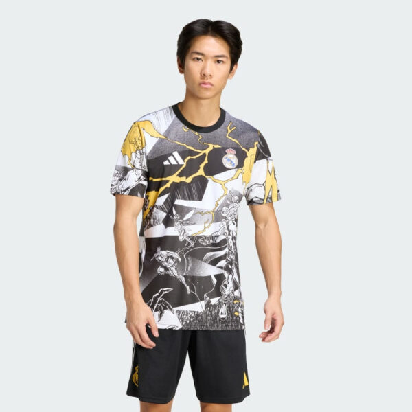 Young man modeling a Real Madrid graphic sports jersey with black-and-yellow lightning design and black shorts against a light gray background.