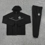 Black Inter Milan tracksuit laid flat: hooded zip-up jacket with crest and a matching pair of joggers on a gray carpet surface.