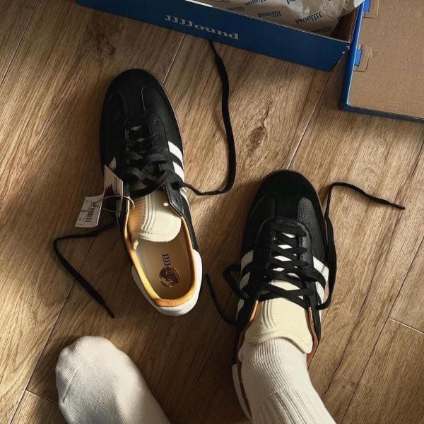 Pair of black-and-white sneakers on a wooden floor beside a blue shoe box, with laces untied.