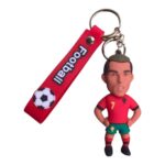 Keychain with a small soccer player figurine in a red jersey and green shorts attached to a red strap with a soccer ball graphic.